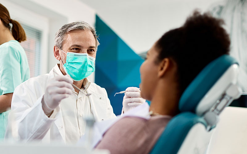 An older male dentist speaks to a female African-american patient