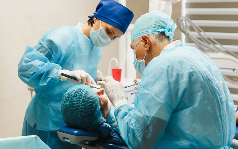 On oral surgeon and surgery assistant perform surgery on a patient